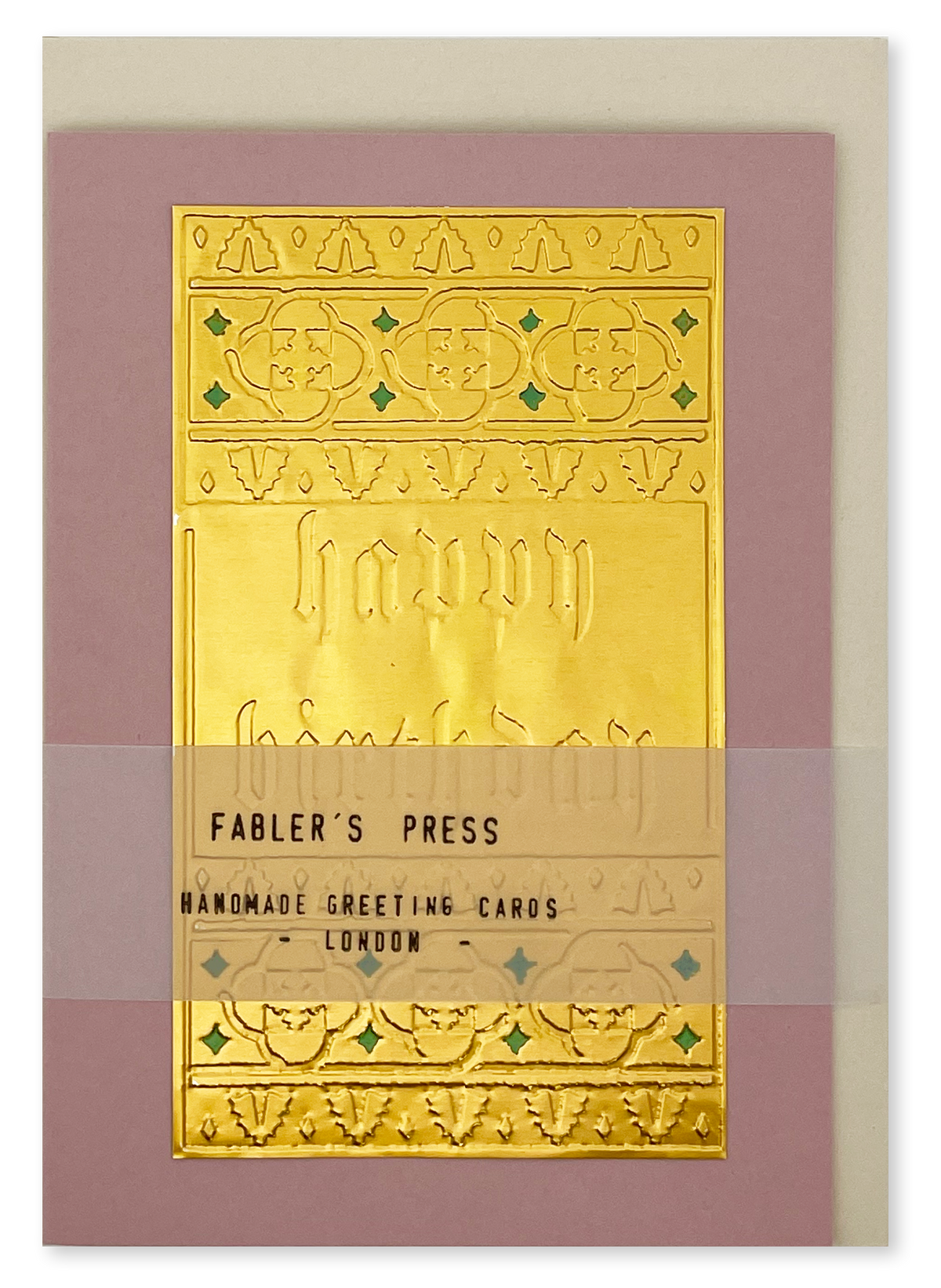 A handmade greeting card from Fabler's Press featuring a large embossed gold foil panel with decorative borders and the words 'Happy Birthday' on a dusty pink background, with a light cream envelope behind it and a translucent belly band packaging.