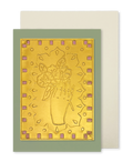 A greeting card with a metallic gold foil design of a hand holding a bouquet of flowers, set against a sage green border with small pink geometric accents. A cream-colored envelope is positioned behind the card.