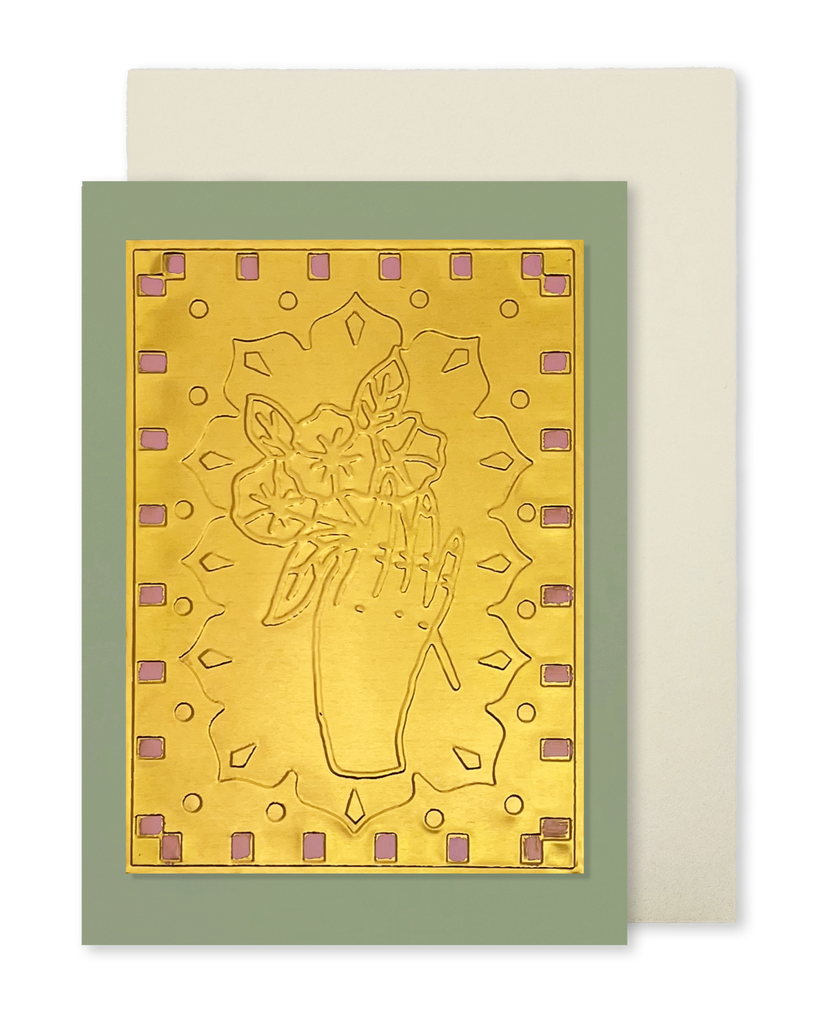 A greeting card with a metallic gold foil design of a hand holding a bouquet of flowers, set against a sage green border with small pink geometric accents. A cream-colored envelope is positioned behind the card.