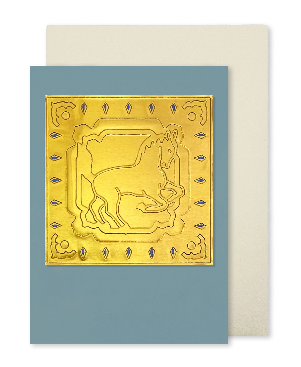 A greeting card with a dusty blue cover featuring an embossed gold horse design, shown with a cream envelope behind it on a white background.