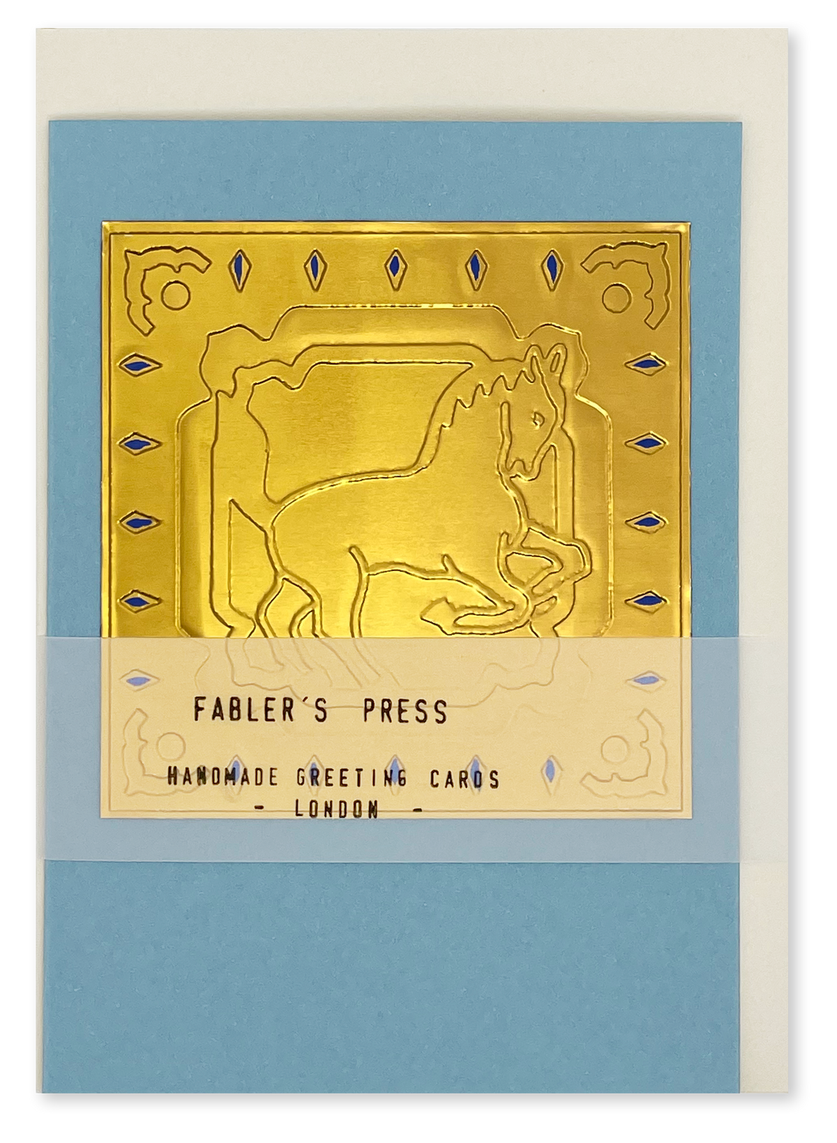 A video of a gold-toned embossed greeting card with horse, surrounded by an ornate patterned border, set against a blue card. Two hands picking it up, opening it to show the ivory white insert, closing it and putting it down. All on a canvas background.