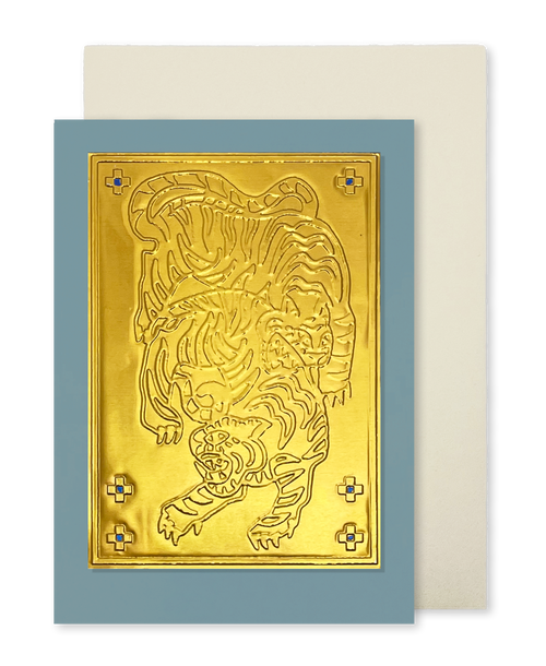 A greeting card by fabler's Press with a raised gold tiger design on a muted blue cardstock, shown with a plain off-white envelope behind it on a white background.
