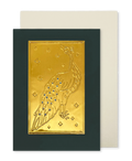 A greeting card with a dark green border and a central gold foil embossed peacock design with blue jewel accents, shown with a cream envelope behind it on a white background.