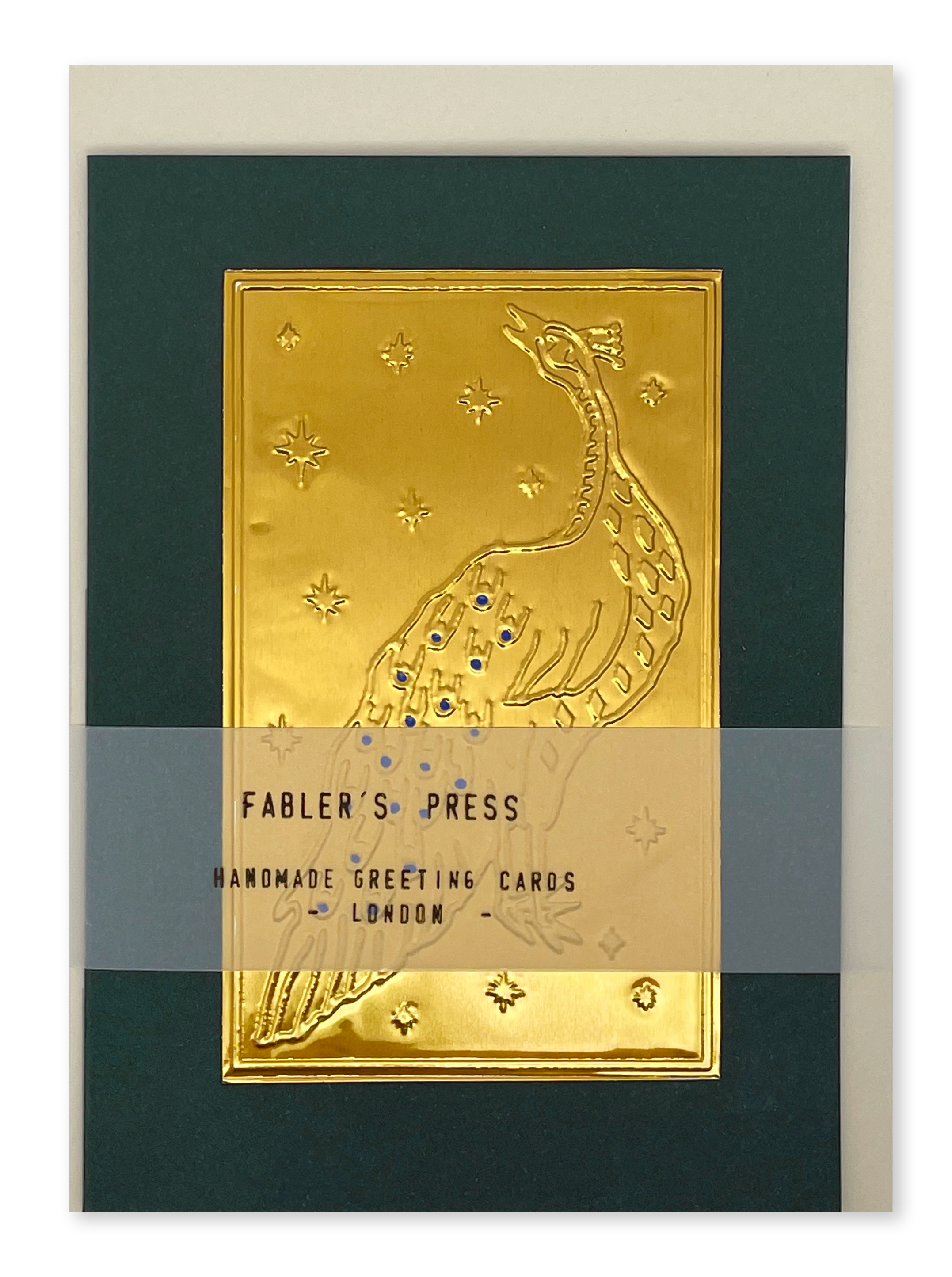 A handmade greeting card from Fabler's Press featuring a raised gold foil peacock design on a dark green background, with a cream envelope and a semi-transparent horizontal packaging label across the centre.