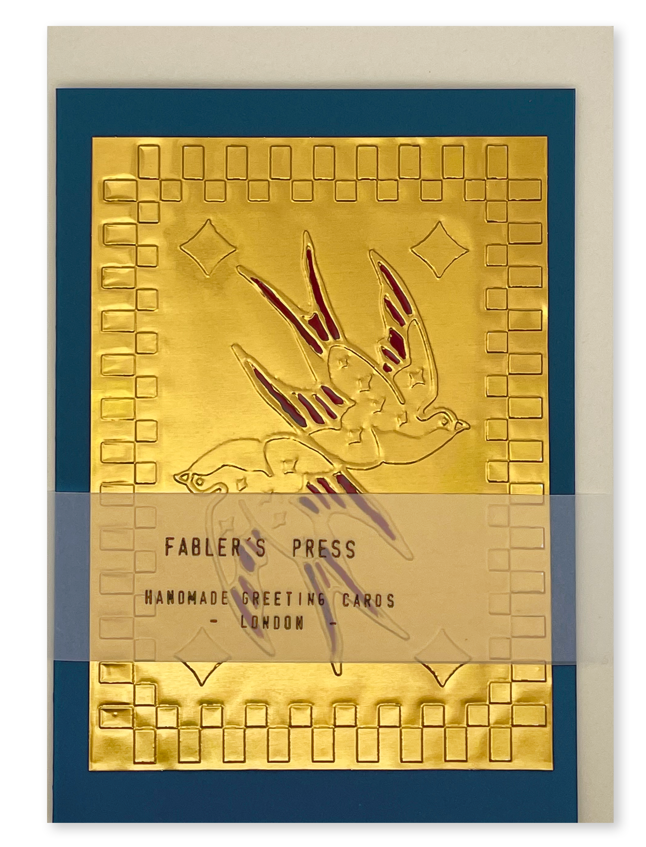 A Fabler's Press handmade greeting card shown on a almond white envelope background, featuring a square  patterned gold foil-engraved card with with two symmetrical swallows a blue border.